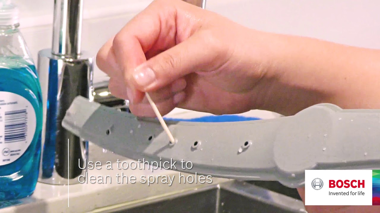 Using a toothpick to clean the spray holes on a Bosch dishwasher spray arm to maintain optimal performance