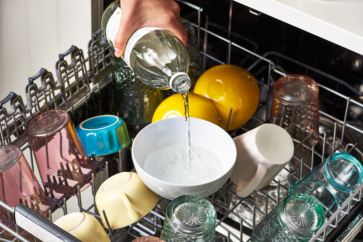 Pouring white vinegar into a dishwasher-safe bowl inside the dishwasher to help deep clean and deodorise during the cleaning cycle